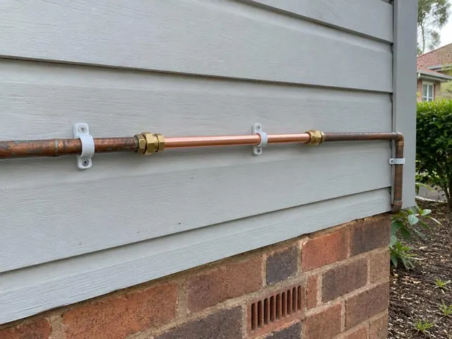 Repaired copper water pipe on exterior weatherboard wall above brickwork in Lindfield