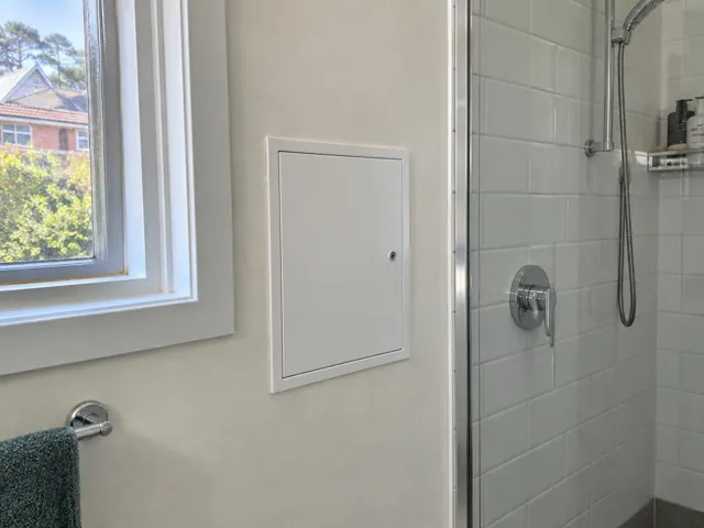 Neat access panel beside a shower in a tiled bathroom with a window and towel rail in Willoughby